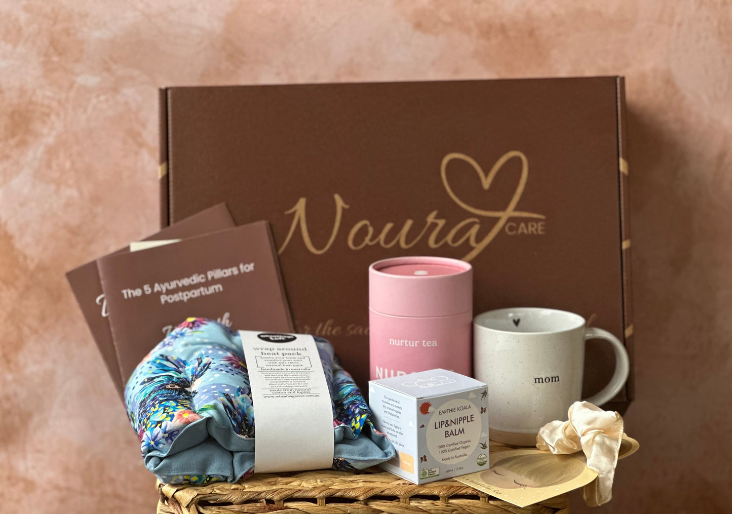 Gift basket with 'Noura Care' branded box, mug, and other items on a textured surface.